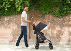 Man pushing a black stroller against a brick wall with greenery 6-365 Plus Stroller