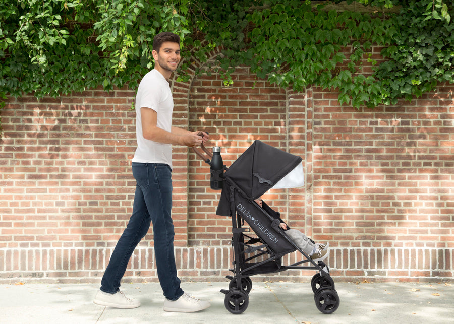 Man pushing a black stroller against a brick wall with greenery 6-365 Plus Stroller