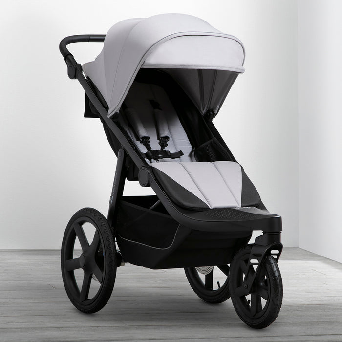 A man is pushing a black Jeep PowerGlyde Pro Jogging Stroller with a child reclined in it, walking on a trail in a forest. 1-Jeep PowerGlyde Pro Jogging Stroller