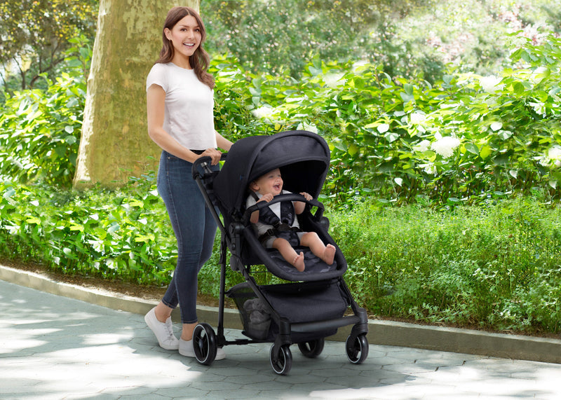 Woman pushing a black stroller with a child in it, walking on a path in a park. 14-babyGap 2-in-1 Carriage Stroller