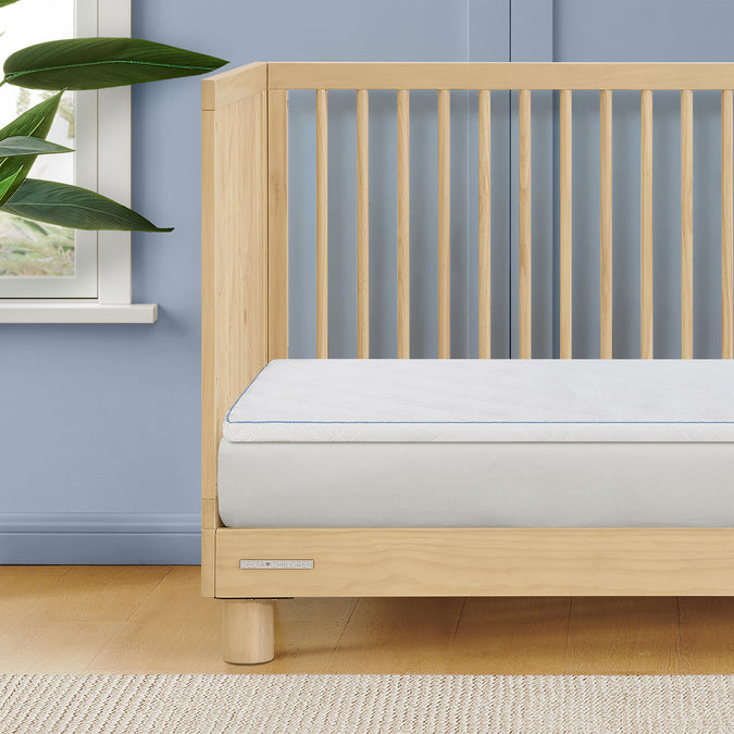 Wooden crib with a white mattress against a blue wall 15-Breeze Breathable Crib Mattress Topper