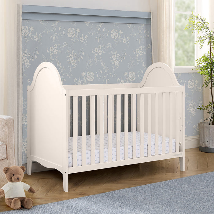 White crib in a room with floral wallpaper and a teddy bear on the floor. 0-Willa 4-in-1 Convertible Crib