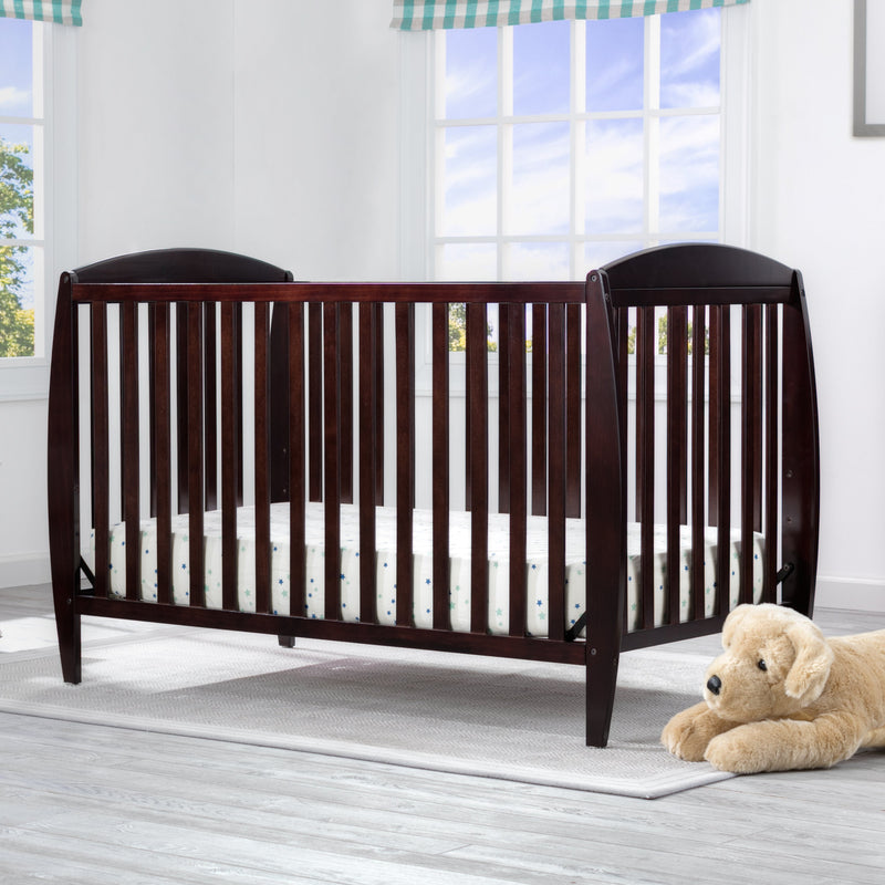 Wooden crib in a bright room with a teddy bear on the floor.
