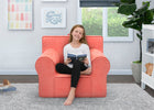 Young girl sitting on a coral chair reading a book in a room with decorative elements. 19-XL Cozee Foam Chair - Perfect Size for Kids Ages 18 Months - 12 Years+