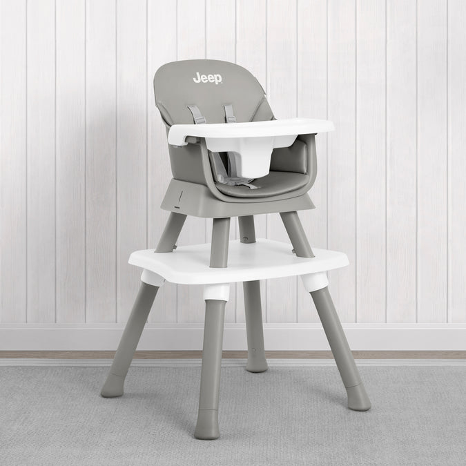 A gray and white Jeep high chair with a matching footrest, set against a white paneled wall and gray carpet. 51-Milestone 6-in-1 High Chair
