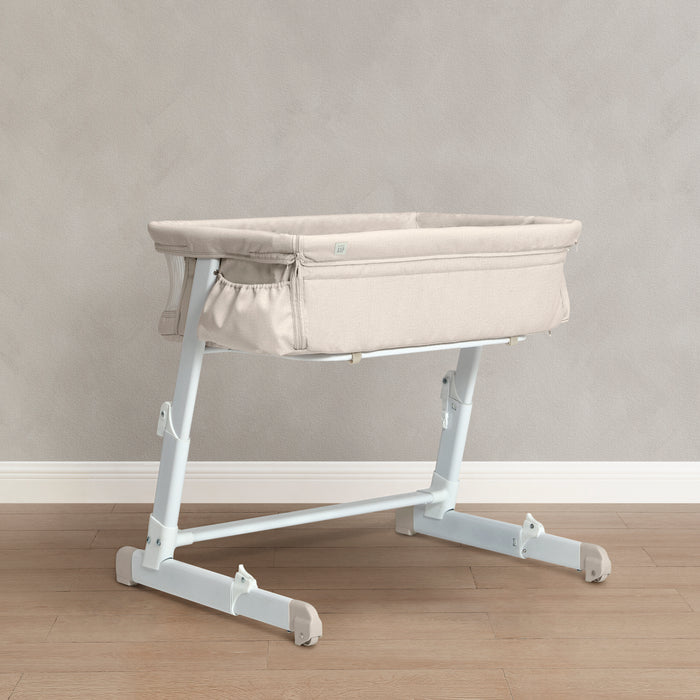 Baby bassinet with adjustable stand on a wooden floor against a gray wall 0-babyGap Deluxe Whisper Bedside Bassinet