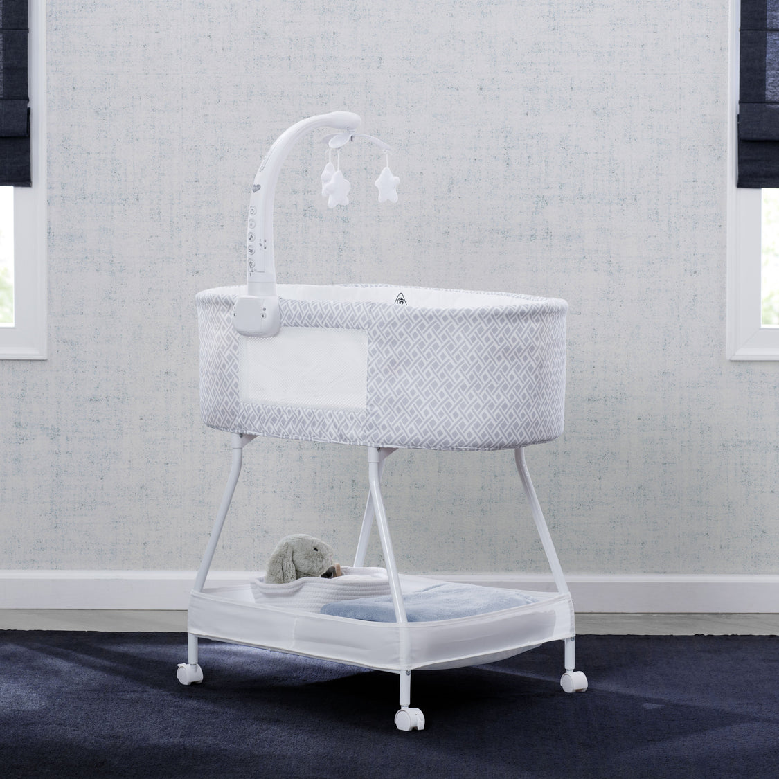 White crib with gray textured cover in a room with gray walls and dark carpet.