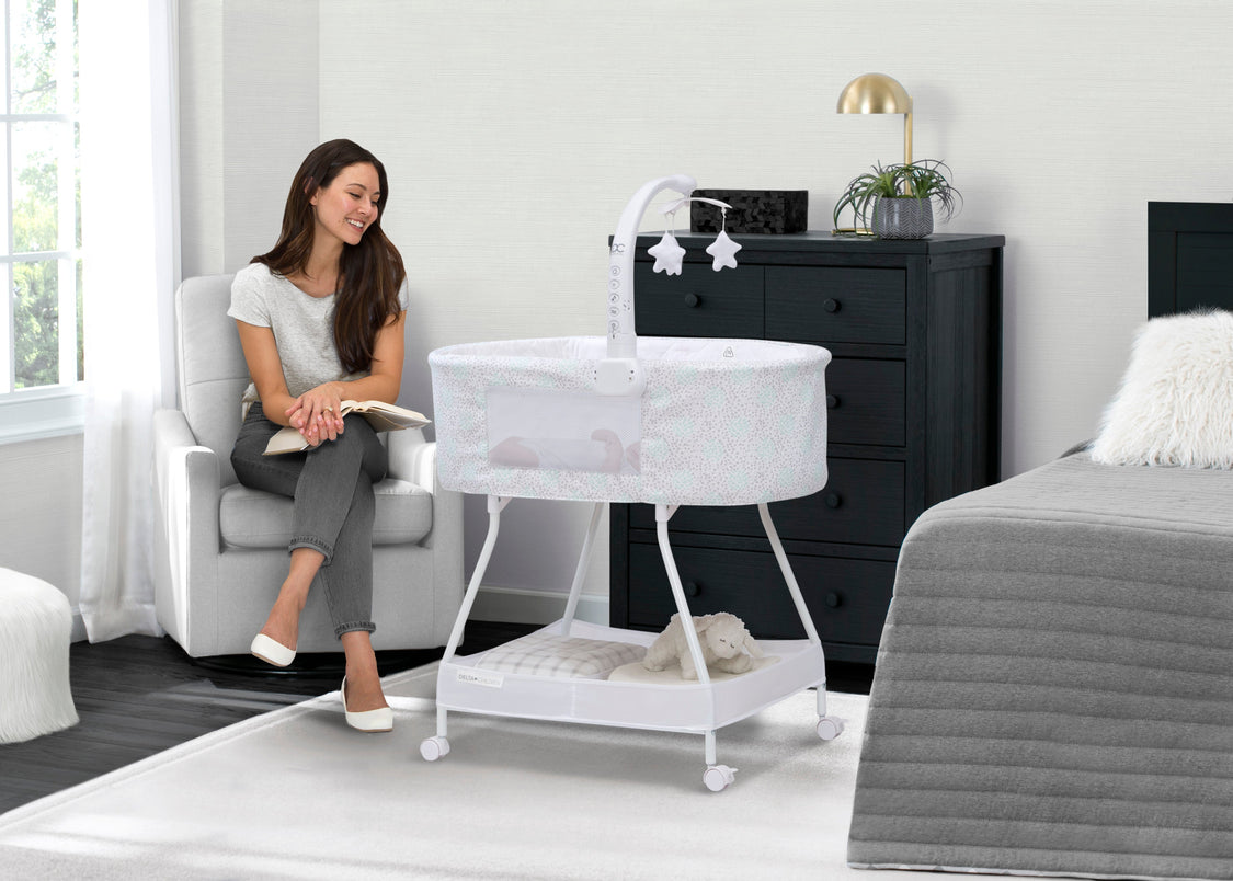 Woman sitting in a modern bedroom with a baby bassinet and dresser.