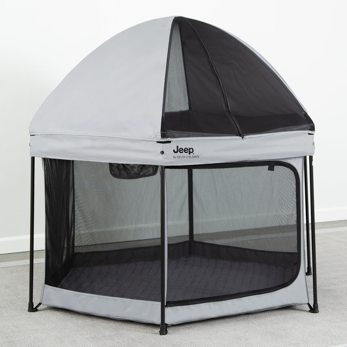 A Jeep branded hexagon-shaped pop-up play yard with a removable canopy and mesh netting on the sides, in a color scheme of gray and black.