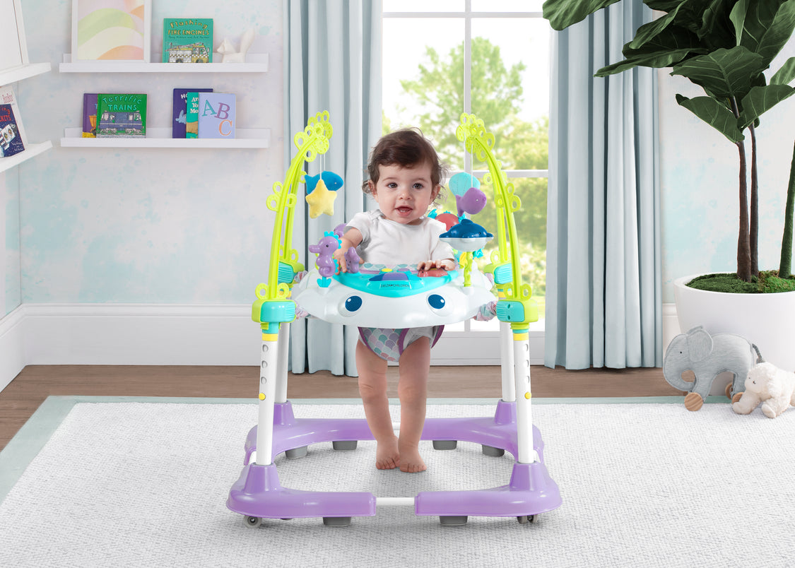 Baby in a colorful baby walker in a room with toys and plants