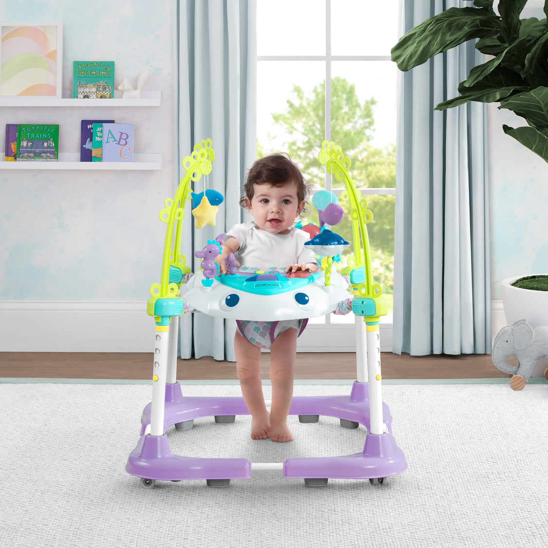 Child in a colorful baby walker in a room with toys and plants
