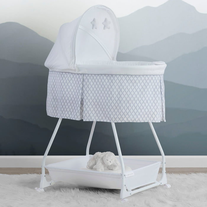A white Delta Children Deluxe Soothing Dreams Bassinet with mesh sides, an attached electronic pod, and a plush star hanging above the bassinet. 0-Deluxe Soothing Dreams Bassinet