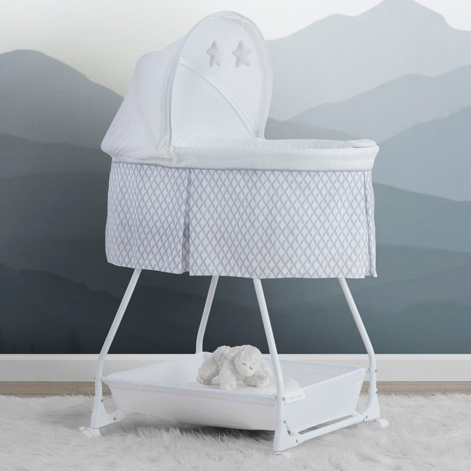 A white Delta Children Deluxe Soothing Dreams Bassinet with mesh sides, an attached electronic pod, and a plush star hanging above the bassinet. 23-Deluxe Soothing Dreams Bassinet