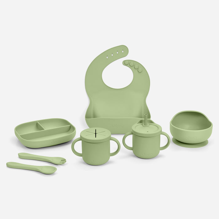 A sage green silicone baby feeding set arranged on a light gray background, including a bib, divided tray, two handled cups with lids and straws, a bowl with a suction base, and two spoons. 0-100% Silicone 10-Piece Baby Feeding Set