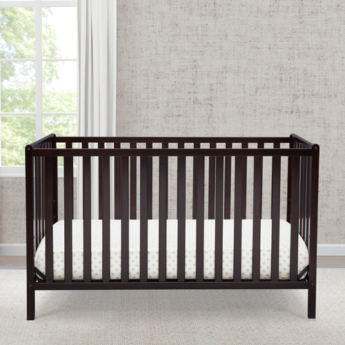 Black crib with white mattress in a room with large windows and gray walls.