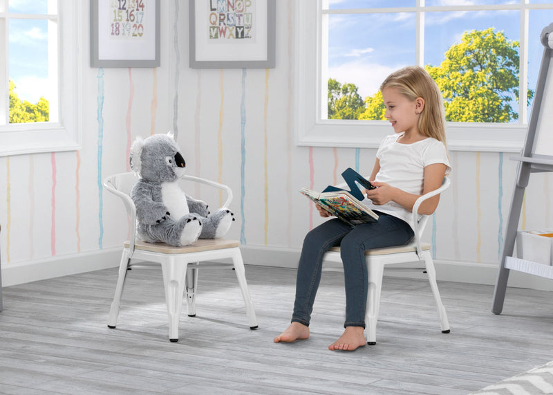 Young girl sitting on a chair with a koala plush toy, reading a book in a bright room.
