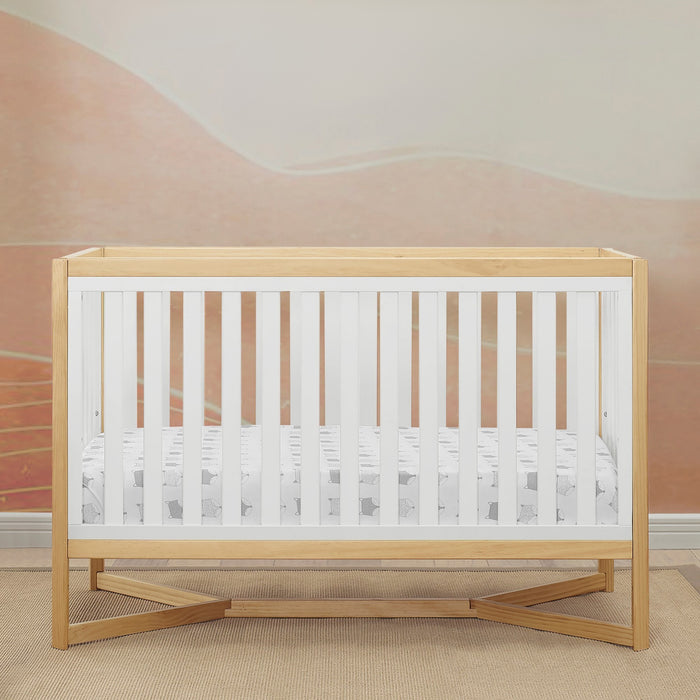 Wooden crib with white mattress in a room with pink walls. 2-Tribeca 4-in-1 Convertible Crib