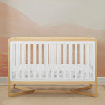 Wooden crib with white mattress in a room with pink walls.