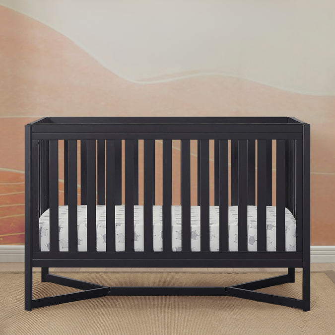 Black crib with a white mattress in a room with a pink wall. 21-Tribeca 4-in-1 Convertible Crib