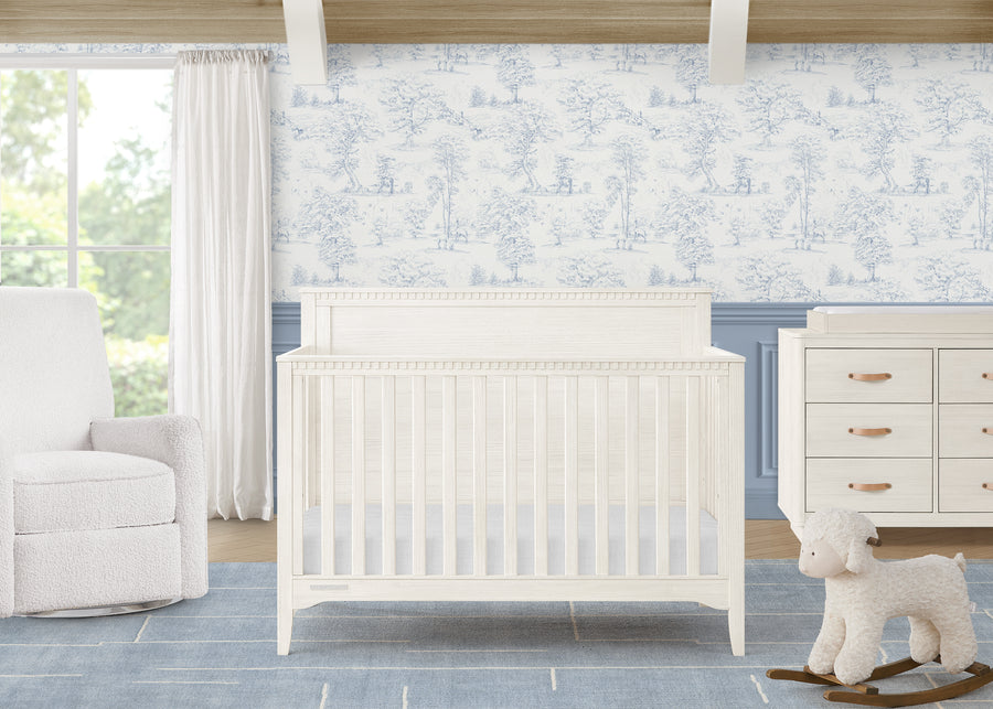 Nursery room with white crib, dresser, and chair against a floral wallpaper wall. 2-Kendall 6-in-1 Convertible Crib