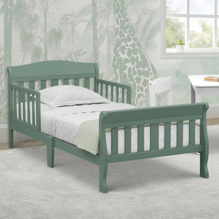 Green children's bed with white bedding in a room with patterned wallpaper and a window. 0-Canton Toddler Bed