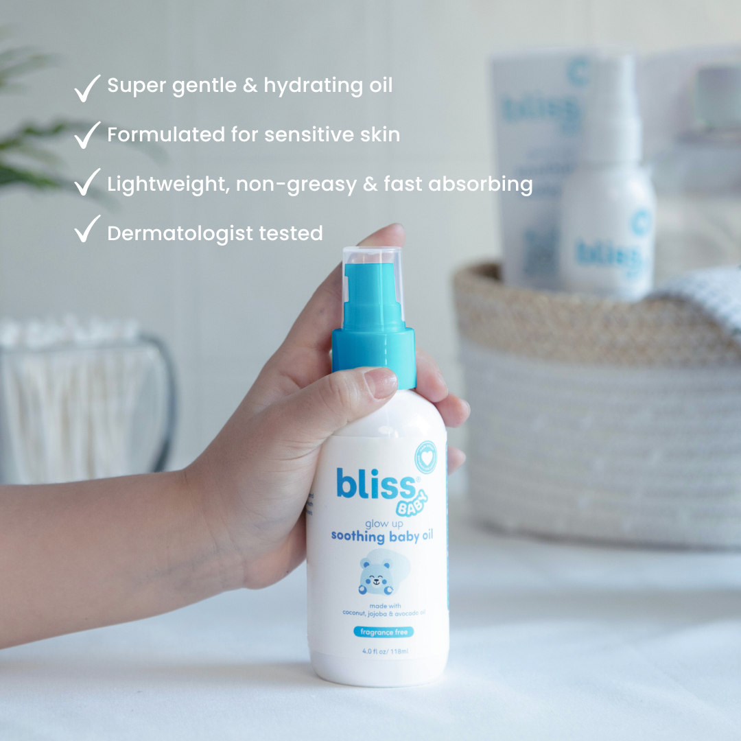 Hand holding a bottle of Bliss Baby oil with product details on a neutral background