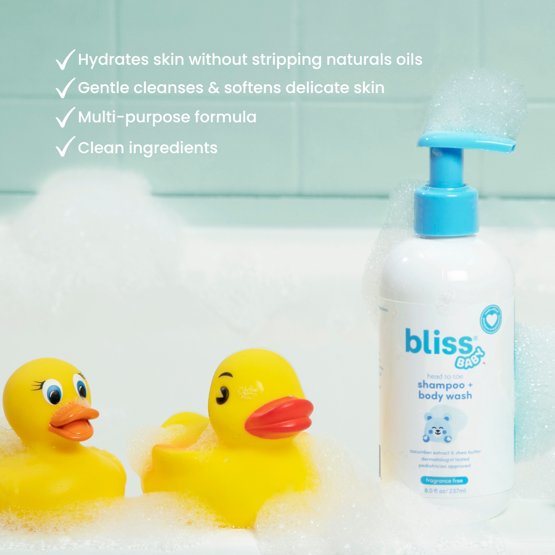 Bottle of bliss baby shampoo and body wash with two yellow rubber ducks in a bathtub.