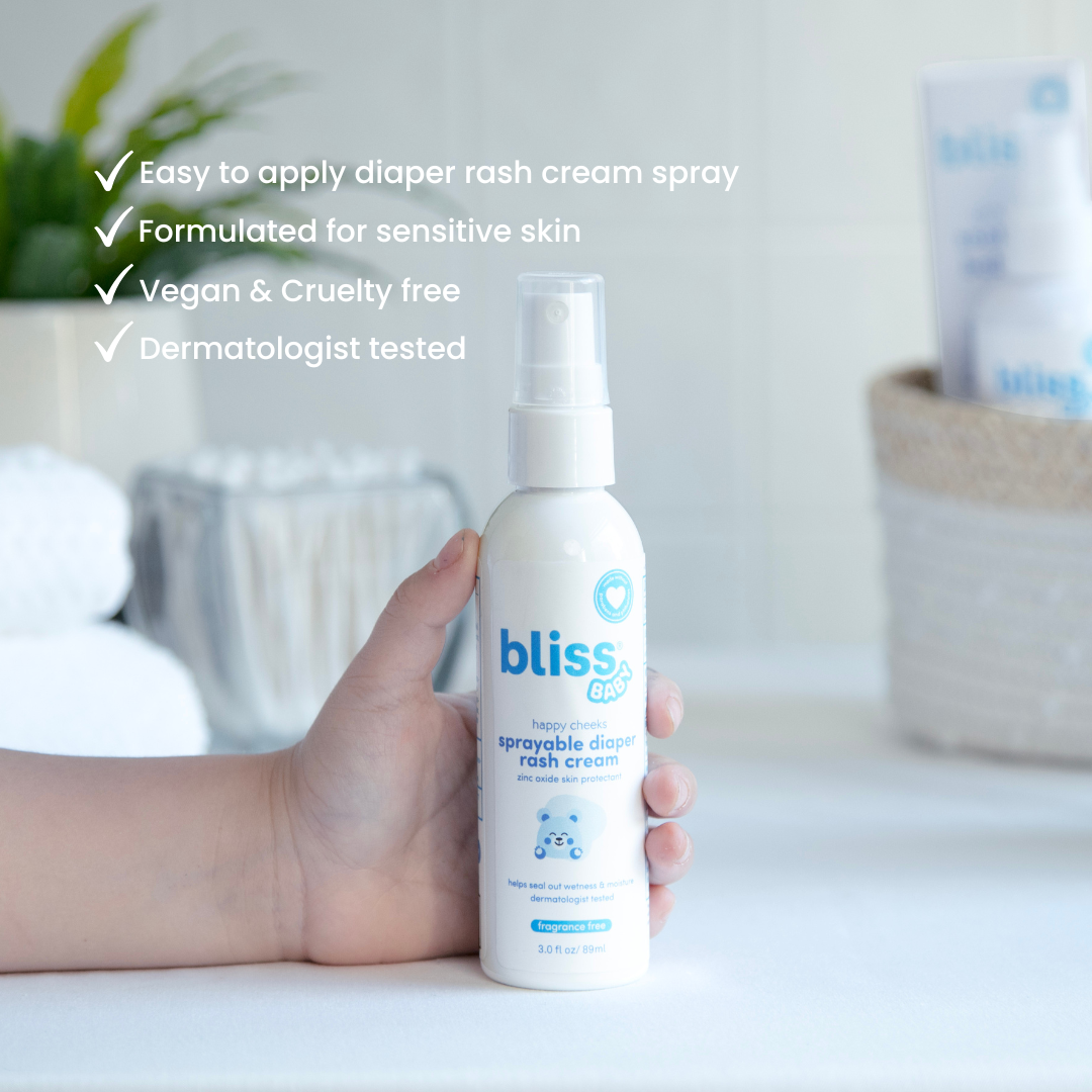 Hand holding a bottle of Bliss diaper rash cream spray with product features listed.