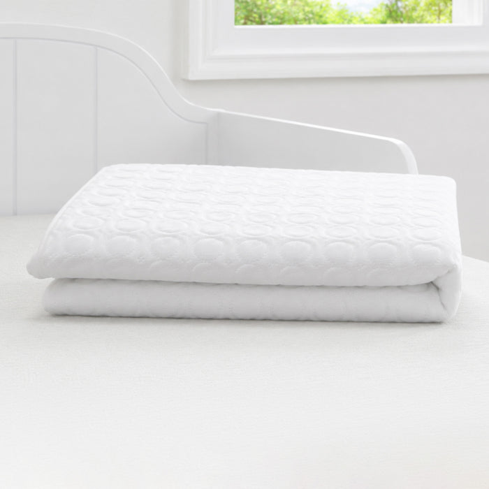 A folded white quilted mattress protector or comforter set on a white bed frame, with a bright window in the background. 1-Cooling Crib Mattress Protector