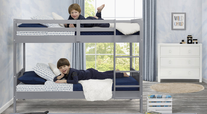 Two children lying on a gray bunk bed in a room with white walls and a window. 3-Bunk Bed Collection