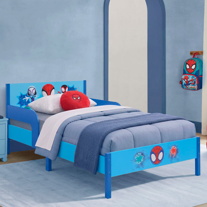 A children's bed with a bright blue frame decorated with Spider-Man character graphics, styled with blue bedding, a red round pillow, and a Spider-Man backpack hanging on the wall in a matching blue bedroom. 1-Spidey and His Amazing Friends Wood Twin Bed with Removable Guardrails