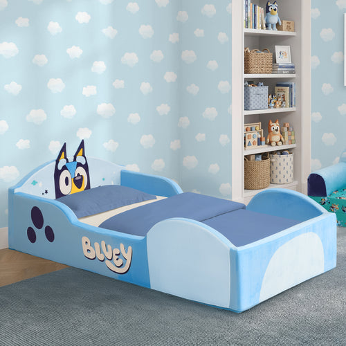 A children's bed styled like Bluey, featuring a light blue and white frame with the character's face on the headboard, blue bedding, and a matching blue patterned wall in a child's bedroom.