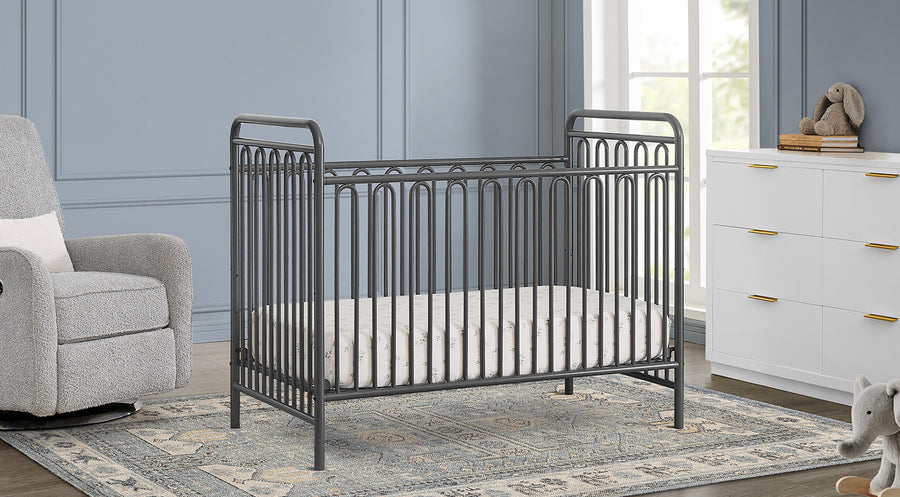 Nursery room with a metal crib, gray armchair, and white dresser. 2-Darcy Collection