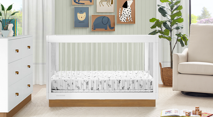 A modern nursery furniture set featuring a brown dresser with a white mattress, a crib with a toddler guardrail, and a glider. The set is displayed in a room with animal-themed wall decor. 1-James Collection