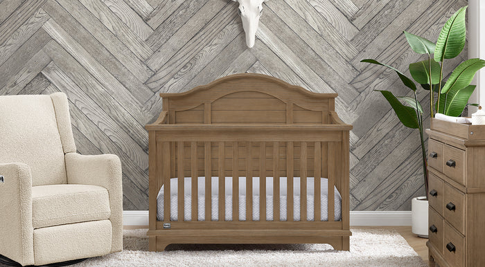 Nursery room with wooden crib, armchair, and dresser against a chevron-patterned wall. 3-Asher Collection