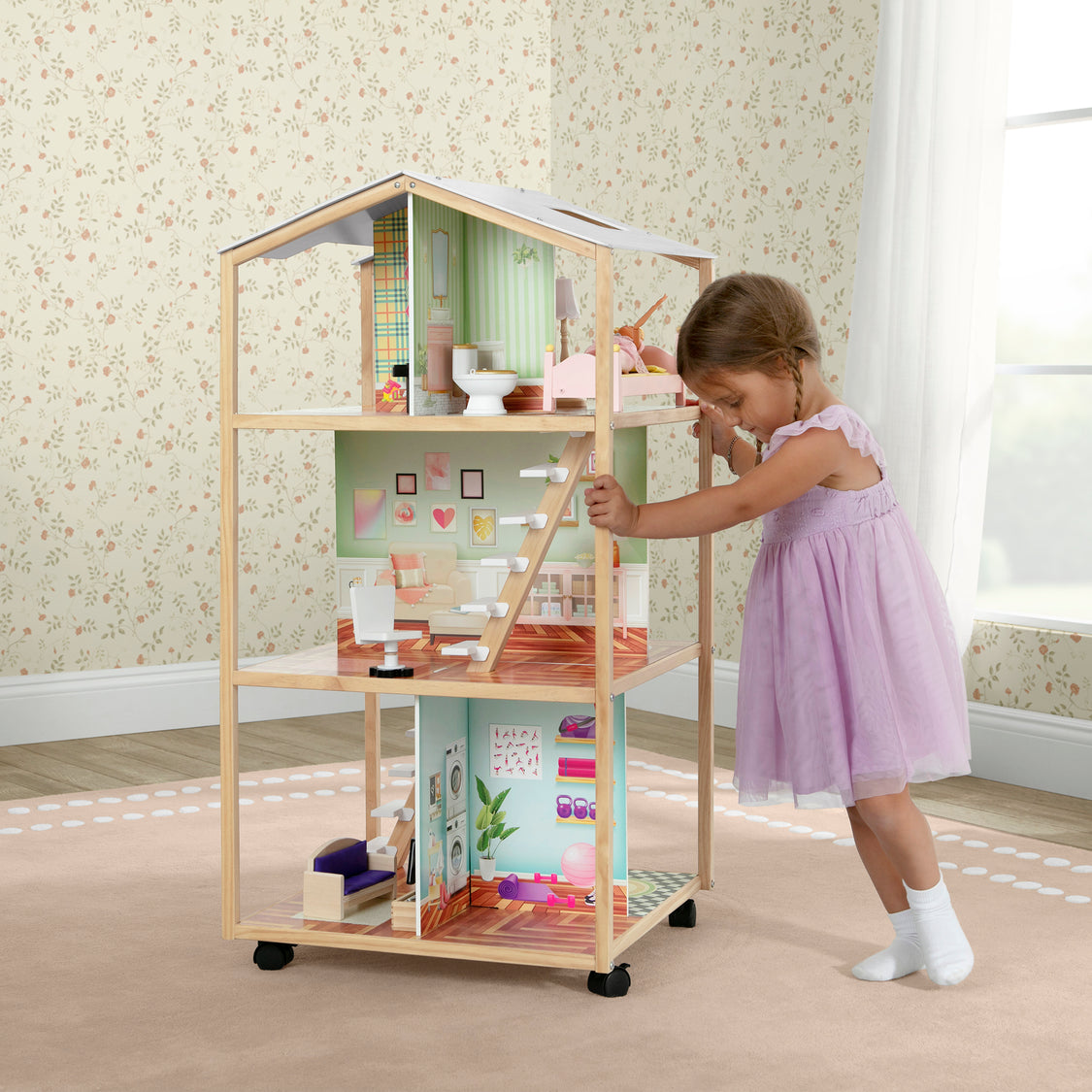 Child playing with a wooden dollhouse in a room with floral wallpaper.