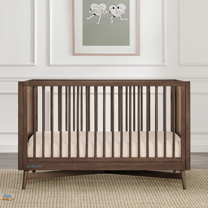 A white Dylan 4-in-1 Convertible Crib with a sleek x-shaped base and round spindles, designed to transform into various furniture pieces as the child grows. 2-Dylan 4-in-1 Convertible Crib