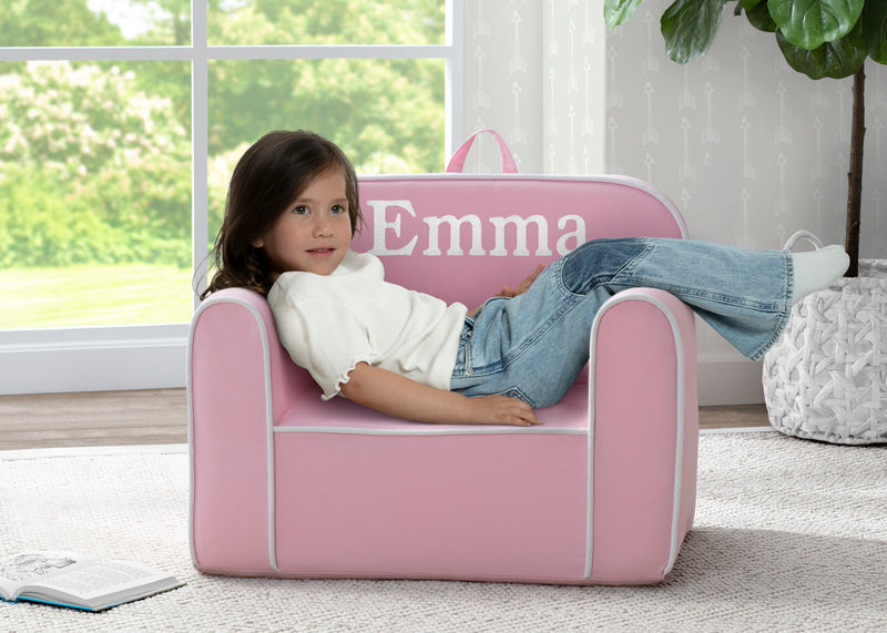 Child sitting on a pink chair with 'Emma' personalized on it, in a bright room.