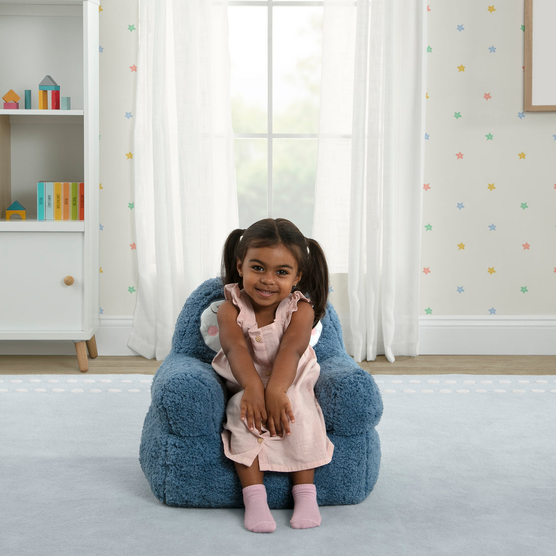 Young girl sitting on a blue bean bag chair in a room with colorful polka dot wallpaper.