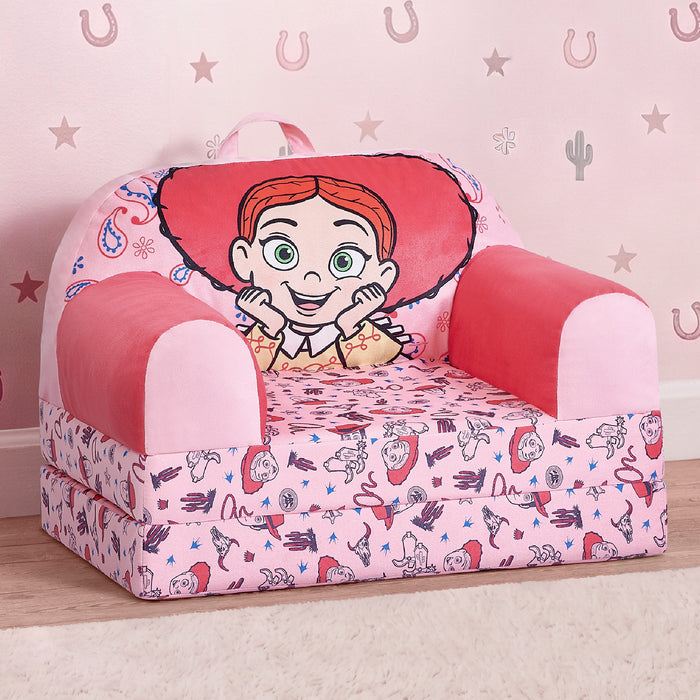 A small pink children's armchair with a cartoon cowgirl graphic on the backrest and a matching printed cushion, photographed in a styled room setting with a patterned pink wall and wood floor. 1-Toy Story Jessie Cozee Buddy Flip-Out Chair