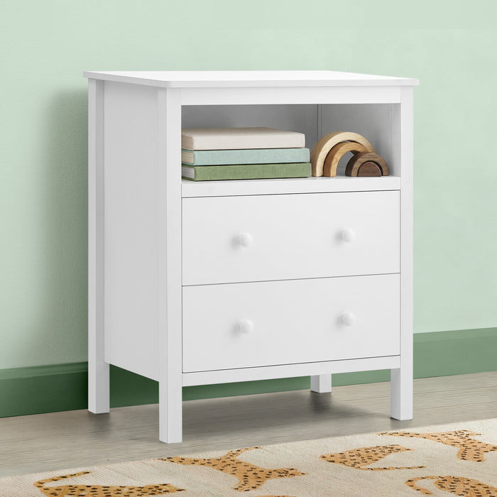 A white three-drawer nightstand with an open top shelf, styled with books and wooden plates, set against a light green wall and wood floor. 0-Dreamer Kids Nightstand with Interchangeable Knobs
