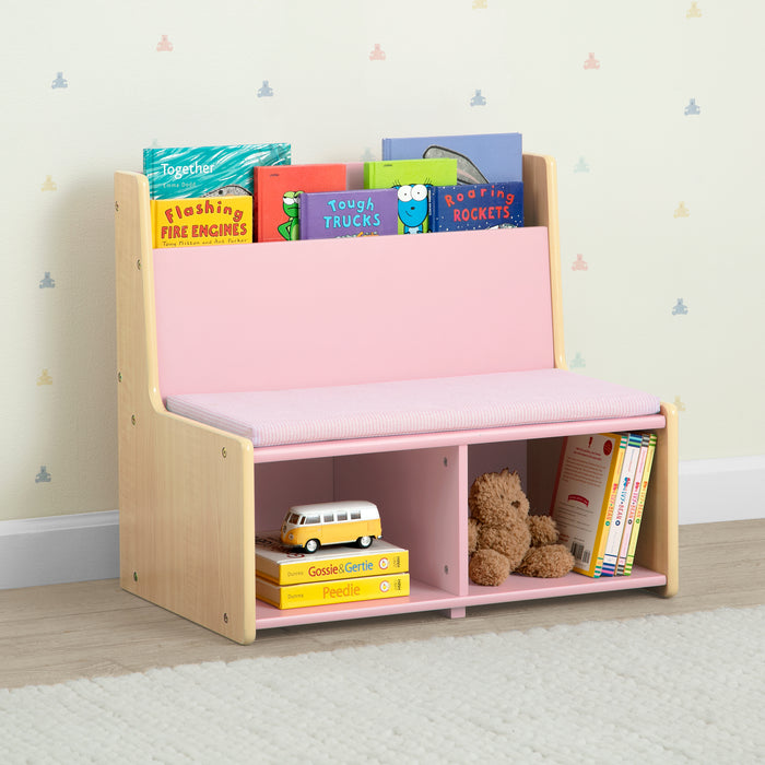 Children's bookshelf with pink top and storage compartments, filled with books and toys, against a light-colored wall. 1-GapKids Reading Nook with Padded Bench