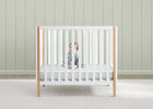 Child in a white crib with wooden frame against a light wooden paneled wall. 14-Twinkle Galaxy 3-inch Mini/Portable Crib Mattress