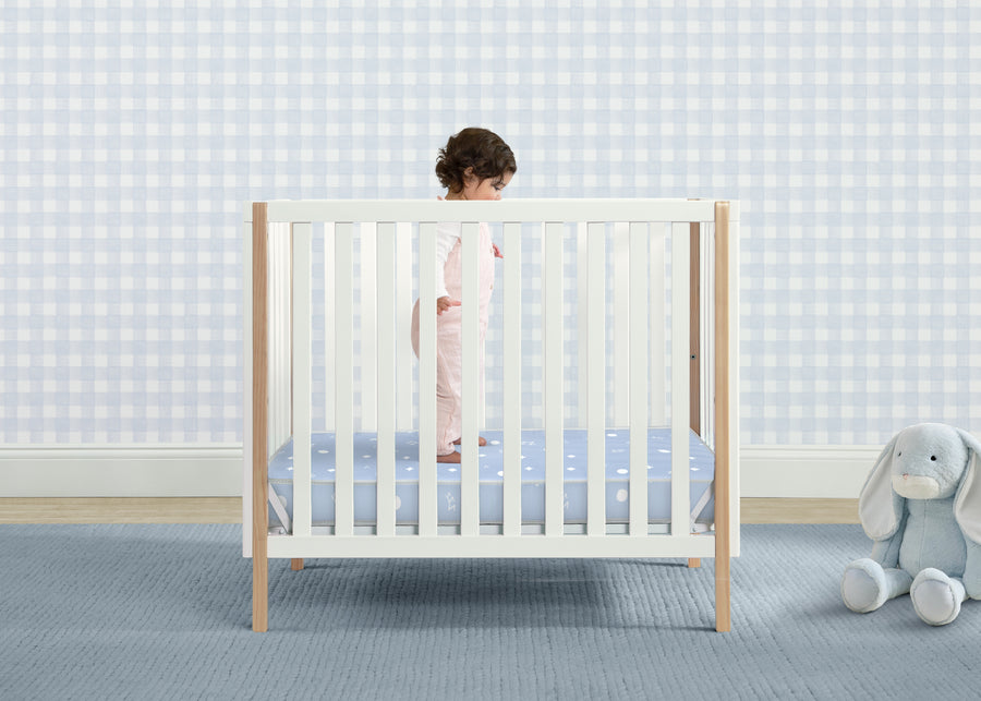 Baby in a crib with a checkered wall and blue rug 14-Simmons Kids® Soothing Nights 3-inch Mini/Portable Crib Mattress