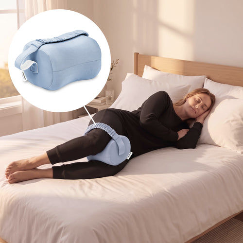 A woman lies on a bed using a light blue pelvic floor support pillow, with a circular inset showing the pillow alone. The room has white bedding, a wooden headboard, and soft natural light.