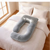 A U-shaped baby support pillow in a soft gray velvet fabric, displayed on a neatly made bed with white sheets and pillows in a bright bedroom. 44-U-Shaped Pregnancy Pillow with Customizable Head Pillow