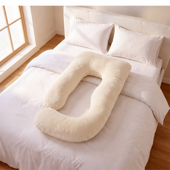 A cream-colored U-shaped body pillow resting on a neatly made bed with white sheets and pillows in a bright bedroom. 48-U-Shaped Pregnancy Pillow