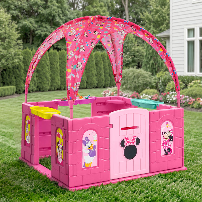 Pink plastic children's playpen with a matching arched canopy featuring cartoon Minnie Mouse prints, set on a green lawn in front of a house. 1-Minnie Mouse Deluxe Playhouse with Canopy