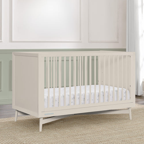 Beige crib in a room with white walls and wooden floor.