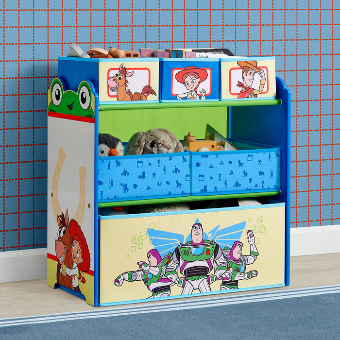 A children's toy storage organizer with colorful cartoon graphics, including Buzz Lightyear on the front drawer and Toy Story characters on the top panels. The unit has three tiers with open shelves and blue fabric bins, shown filled with toys against a blue patterned wallpaper background. 0-Toy Story 6 Bin Design and Store Toy Organizer